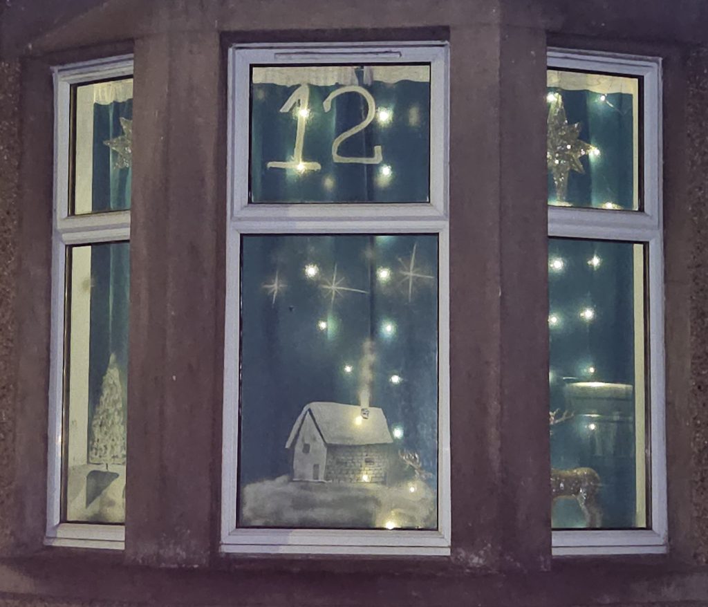 A window with a snow covered house, a Christmas tree and a deer, and the number 12.